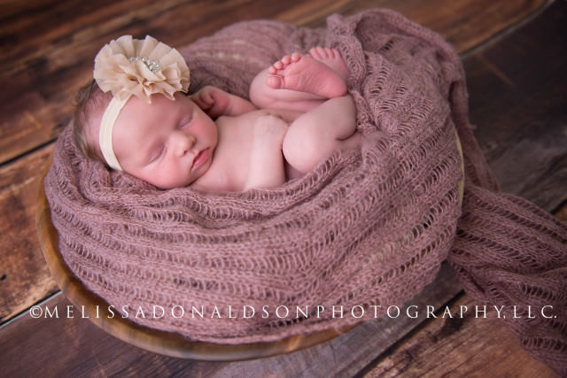 baby in basket with neutral tone bow and with pink wrap