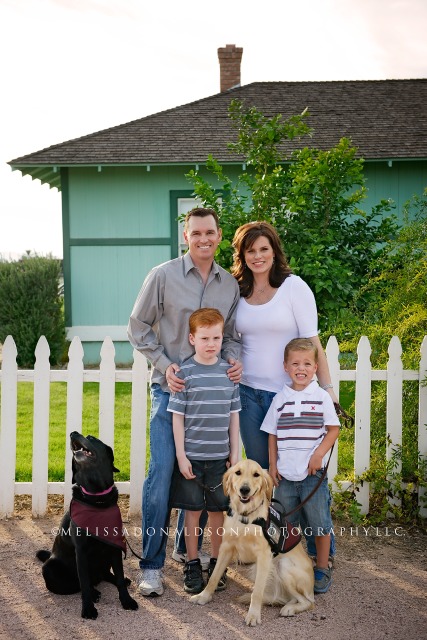 Family with dogs in front of white picket fence