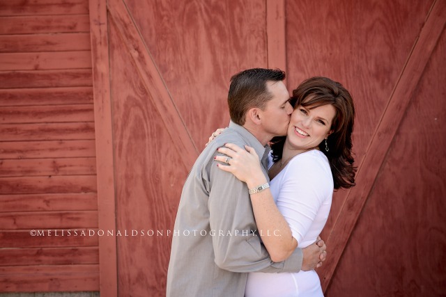 mom kissing dad on cheek in front of red barn