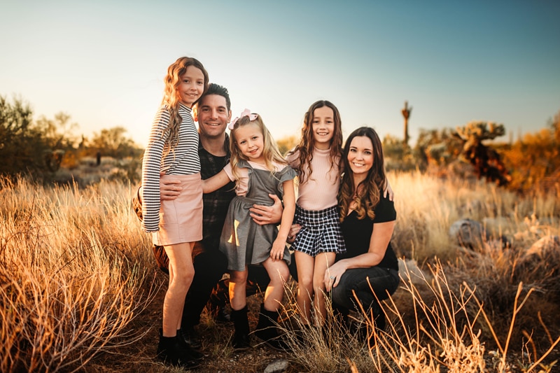 Family Photographer, a mother and father stand with their 3 young daughters in the dry grass
