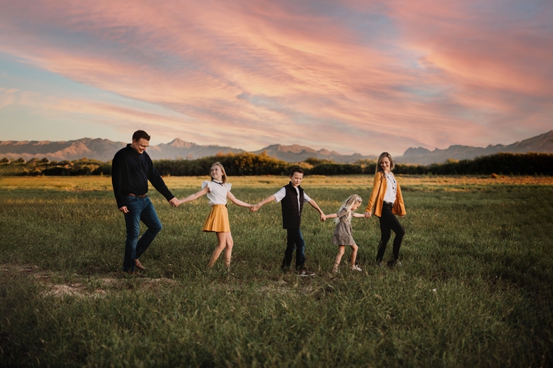 Family Photographer, a family of 5 walks hand in hand through grassy meadow